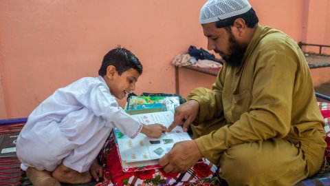 En pappa och hans son sitter mittemot varandra och tittar i en skolbok. 