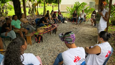 En grupp kvinnor, många i Läkare Utan Gränser-västar, sitter på stolar i en ring. En kvinna står framför dem.