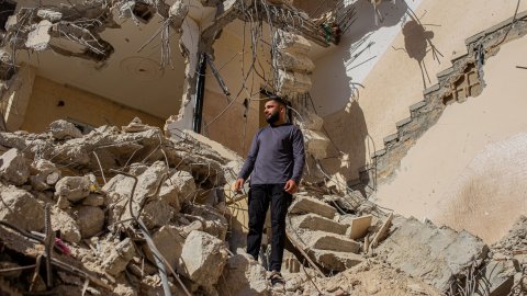 Person står på spillrorna vid ett hus som rasat.