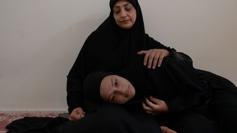 Två svartklädda kvinnor syns där en sitter lutad mot en vägg och den andra ligger i dennes knä.