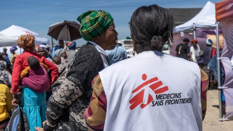 Ryggen på en kvinna med Läkare Utan Gränser-väst som pratar med en annan kvinna utomhus.