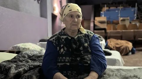 en äldre kvinnar sitter på en tältsäng i en stor sal