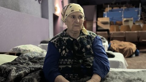 en äldre kvinnar sitter på en tältsäng i en stor sal