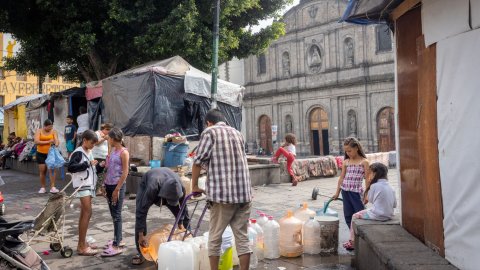 Människor hämtar vatten i stora dunkar på ett torg.
