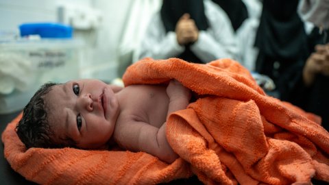 Nyfödd bebis ligger i en handduk och tittar in i kameran.