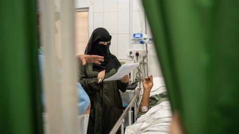 En läkare står vid sjukhussäng och håller i ett papper.