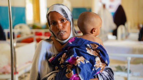 En kvinna tittar in i kameran. Hon håller ett barn över axeln.