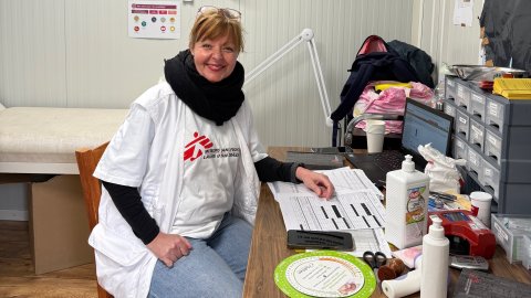 Kvinna med Läkare Utan Gränser t-shirt sitter vid skrivbord, tittar in i kameran och ler