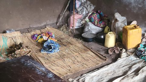 Ett golv med en stråmatta, gula plastdunkar, vita säckar och kläder.