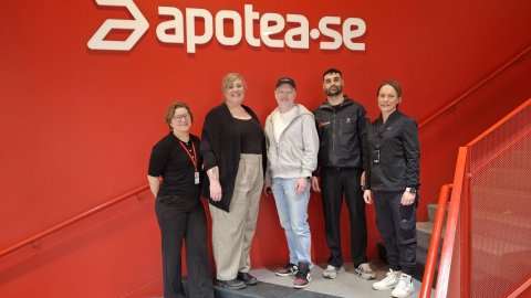 En grupp glada personer framför apoteas logga.