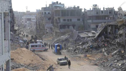 En ambulans parkerad på en väg i ett ruinlandskap. Grupper av människor rör sig längs vägen