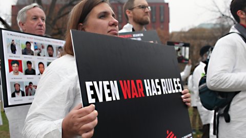 En person håller en skylt där det står even war has rules.