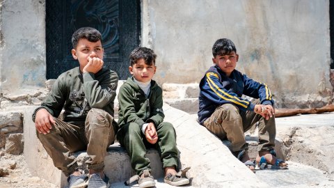 Tre barn som sitter utomhus på stenar/betongblock.