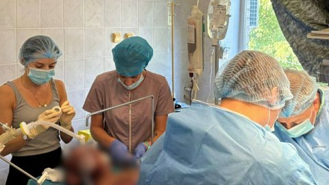 Fyra personer iklädda munskydd varav två blå sjukhusrockar i ett rum på ett sjukhus.