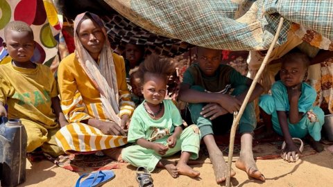 Kvinna och flera barn sitter i ett tält byggt av pinnar och tygstycken