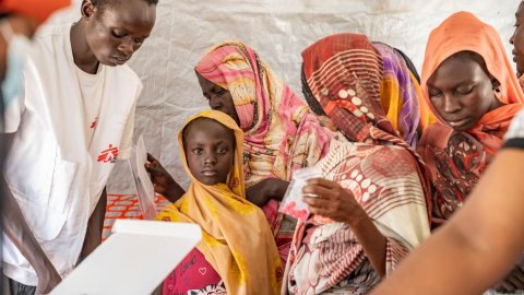 Flicka blickar in i kameran, omgiven av kvinnor och en personal från Läkare Utan Gränser