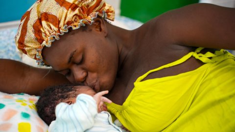 En mamma ligger ner i en säng och pussar sitt nyfödda barn.