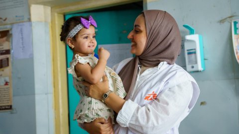En kvinna med vita kläder och Läkare Utan Gränser-väst som håller i ett litet barn.