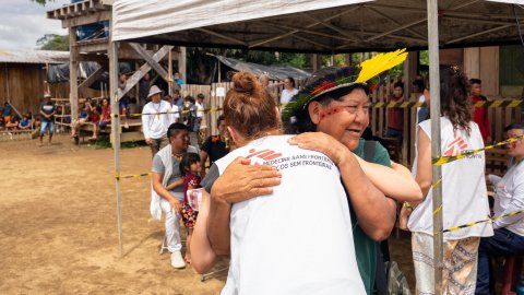 En person i Läkare Utan Gränser-väst kramar om en person med fjäderhuvudbonad och ansiktsmålning.