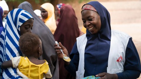 Kvinna i mf-väst ger ett barn näringsgröt på en sked