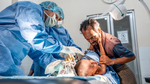 Pojke håller handen på sin pappas kind medan pojken behandlas av två läkare