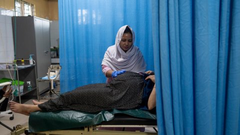 En kvinna undersöker en gravid kvinna som ligger på en sjukhussäng. Den gravida kvinnans huvud döljs bakom ett draperi. 