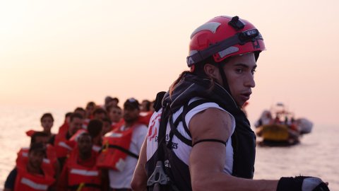 man i hjälm och flytväst på havet, i bakgrunder människor i liten båt