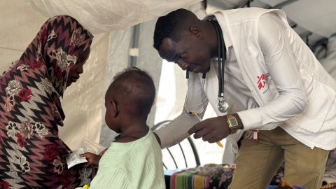 Manlig läkare undersöker barn som sitter med en kvinna