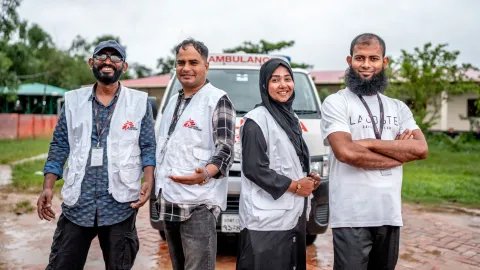 Fyra personer i Läkare Utan Gränser-västar uppradade framför en bil. De ler och kollar in i kameran.