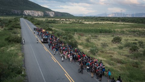 En stor grupp människor går längs en väg med berg i bakgrunden.