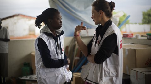 Två kvinnor i vita västar med Läkare Utan Gränsers logotyp står och pratar med varandra.