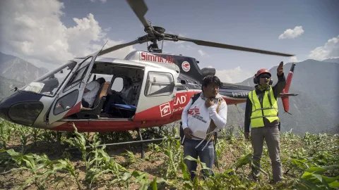 En helikopter som har landat på en höjd och två personer framför helikoptern