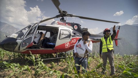 En helikopter som har landat på en höjd och två personer framför helikoptern