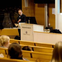 Man på en scen föreläser inför en grupp studenter