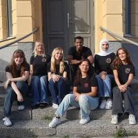 En grupp ungdomar i Friends of MSF t-shirts sittandes på en trappa framför ett hus 