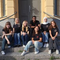 En grupp ungdomar i Friends of MSF t-shirts sittandes på en trappa framför ett hus 