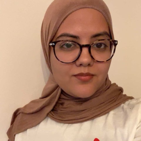 Kvinna tittar in i kameran och har på sig Läkare Utan Gränser-tröja, vit bakgrund.