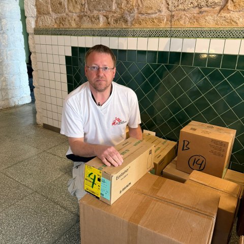 En man sitter vid ett par lådor och tittar in i kameran.