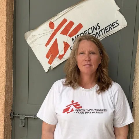 Person i Läkare Utan Gränsers T-shirt står framför en dörr med organisationens logotyp i bakgrunden.