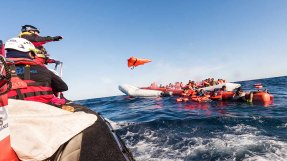 Ett team kastar flytvästar till människor i vattnet bredvid en gummibåt