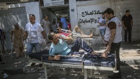 En grupp män på bårar och med kryckor väntar på vård utanför ett sjukhus i Gaza