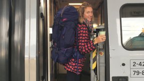 Emily på trappan på ett tåg med stor packning och en kaffekopp i handen
