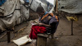En flicka sitter med en bok på en lerväg