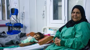 En kvinna sitter bredvid en sjukhussäng där det ligger en flicka, i Qayyrah, Irak,. 