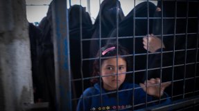 En flicka som bor i lägret Al-Hol i Syrien tittar genom ett stängsel.