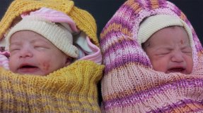 Spädbarnstvillingar ligger bredvid varandra inlindade i färgglada filtar