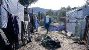 En anställd från Läkare Utan Gränser går, med ryggen mot kameran, på en grusväg genom ett läger på den grekiska ön Samos.