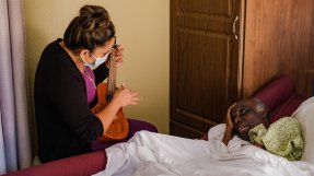 Adelia Patterson spelar på en ukele och sjunger tillsammans med en sängliggande äldre, patient.