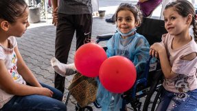 Fyraåriga Hala sitter i en rullstol på al-Awda sjukhuset i Gaza. Hon har två röda ballonger i handen och pratar med sin syster och kusin.