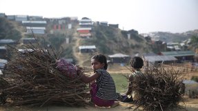 En flicka i flyktinglägret Cox's Bazar, Bangladesh, sitter på huk bredvid en pojke och en hög med grenar och tittar mot kameran.